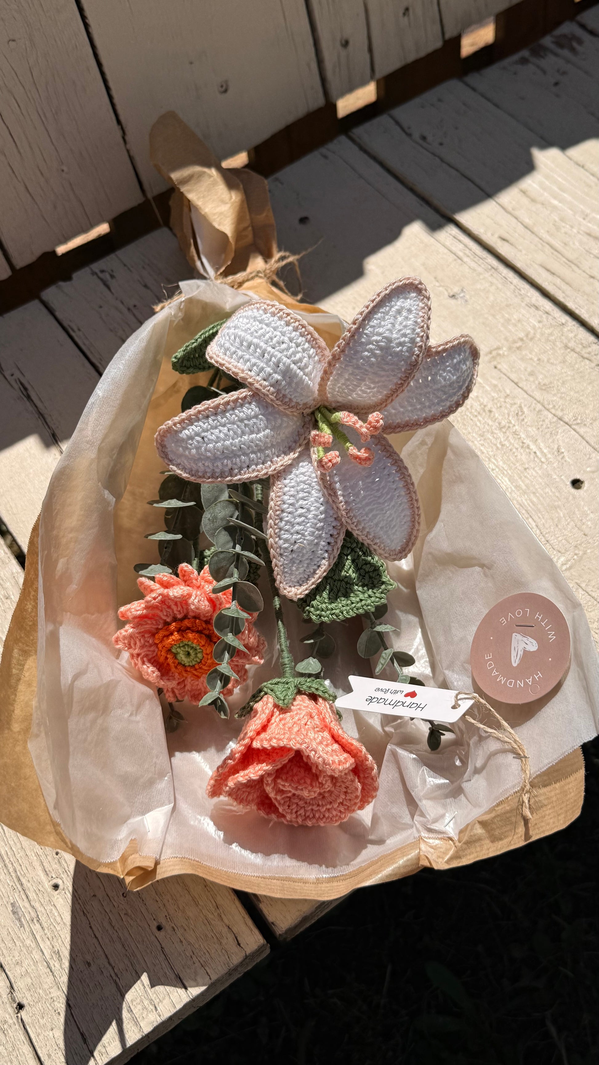 Handgefertigter Blumenstrauß aus der Mama Edeltrud Kollektion mit gehäkelter Lilie und Rosen in Pfirsich-Tönen, liebevoll verpackt in Naturpapier als nachhaltiges Geschenk.