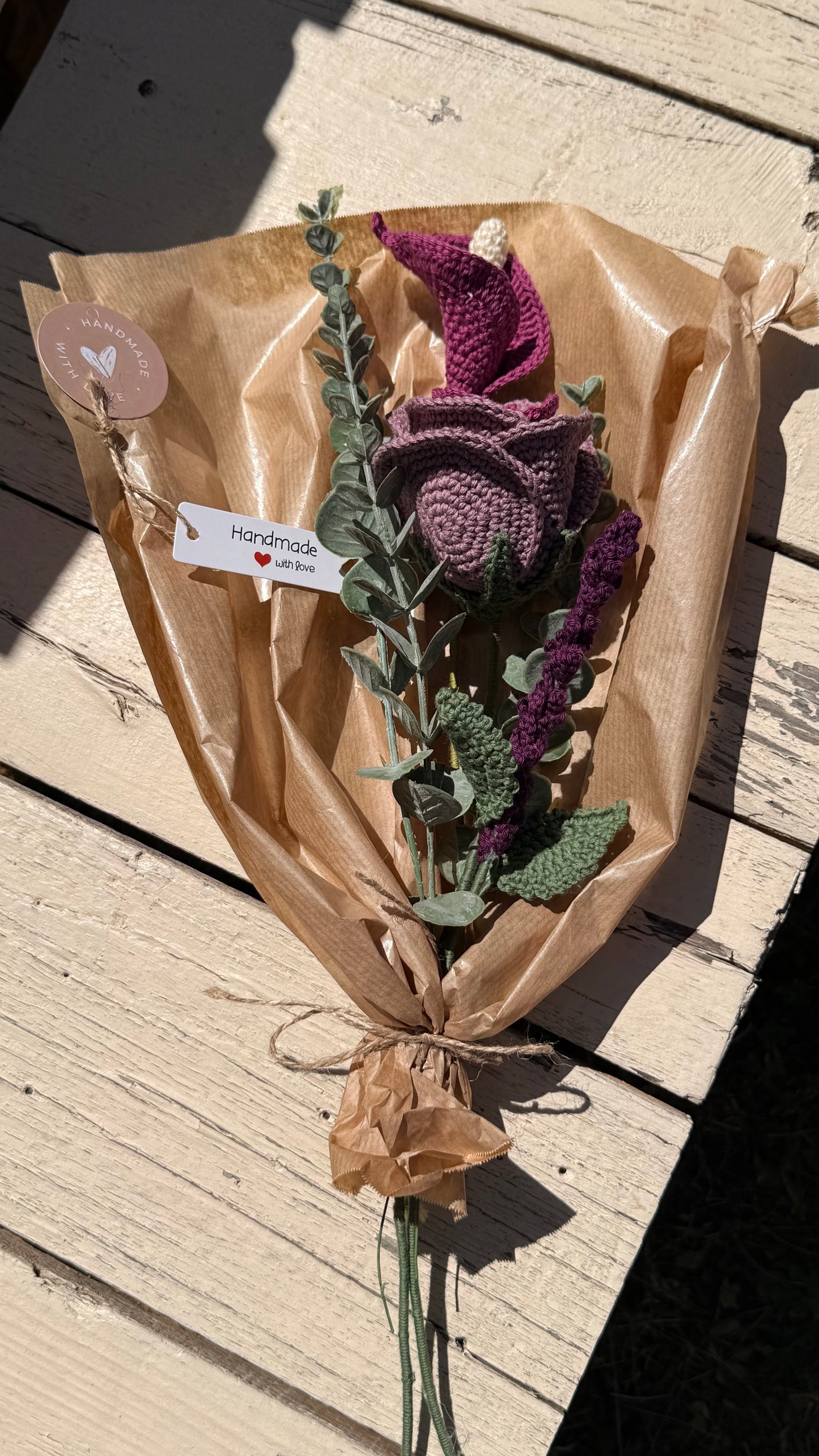 Handgefertigter Blumenstrauß aus der Mama Edeltrud Kollektion mit gehäkelter Calla und Rose in intensiven Beeren- und Violetttönen, elegant verpackt in Naturpapier als nachhaltiges Deko-Geschenk.