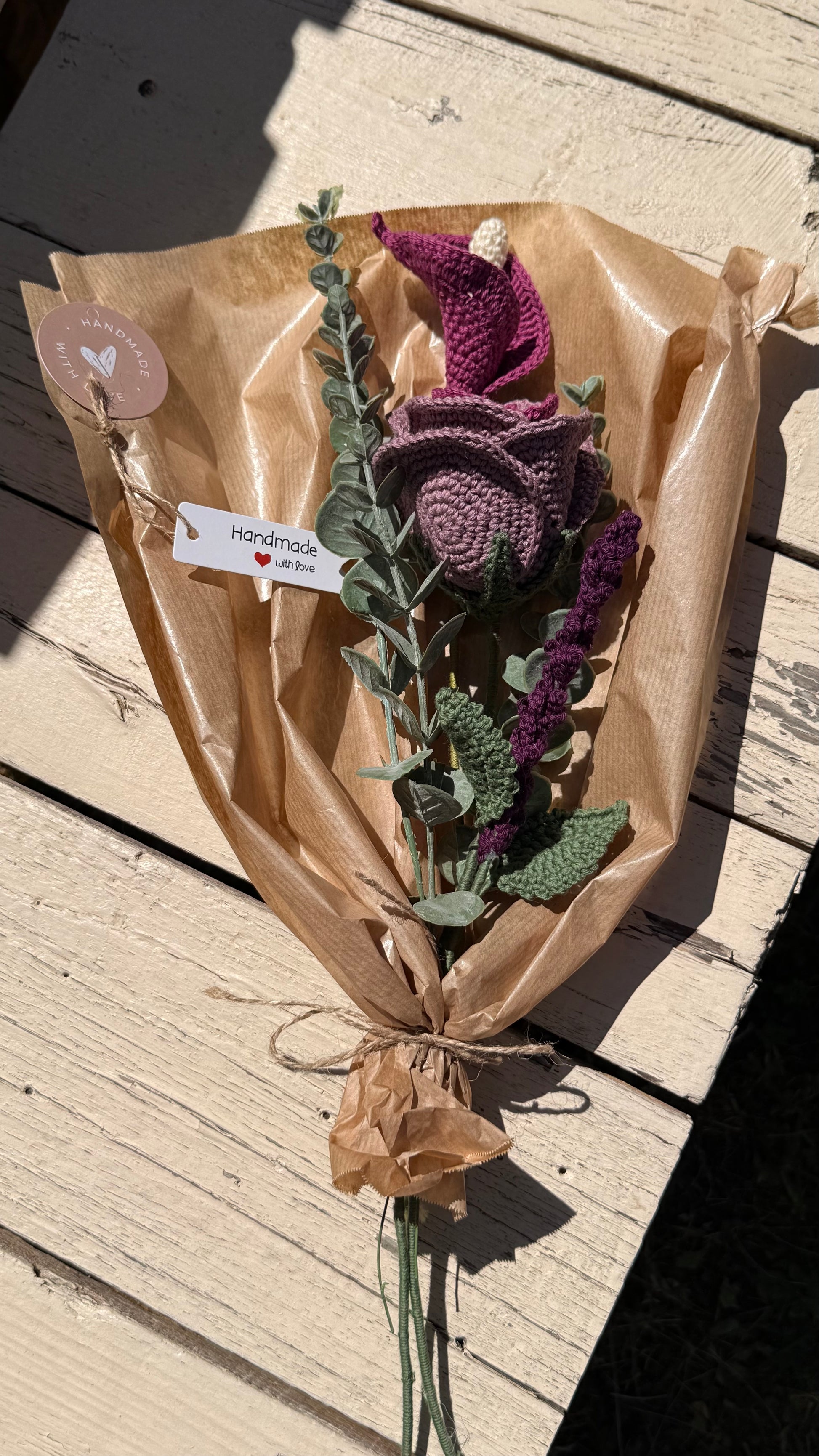 Handgefertigter Blumenstrauß aus der Mama Edeltrud Kollektion mit gehäkelter Calla und Rose in intensiven Beeren- und Violetttönen, elegant verpackt in Naturpapier als nachhaltiges Deko-Geschenk.