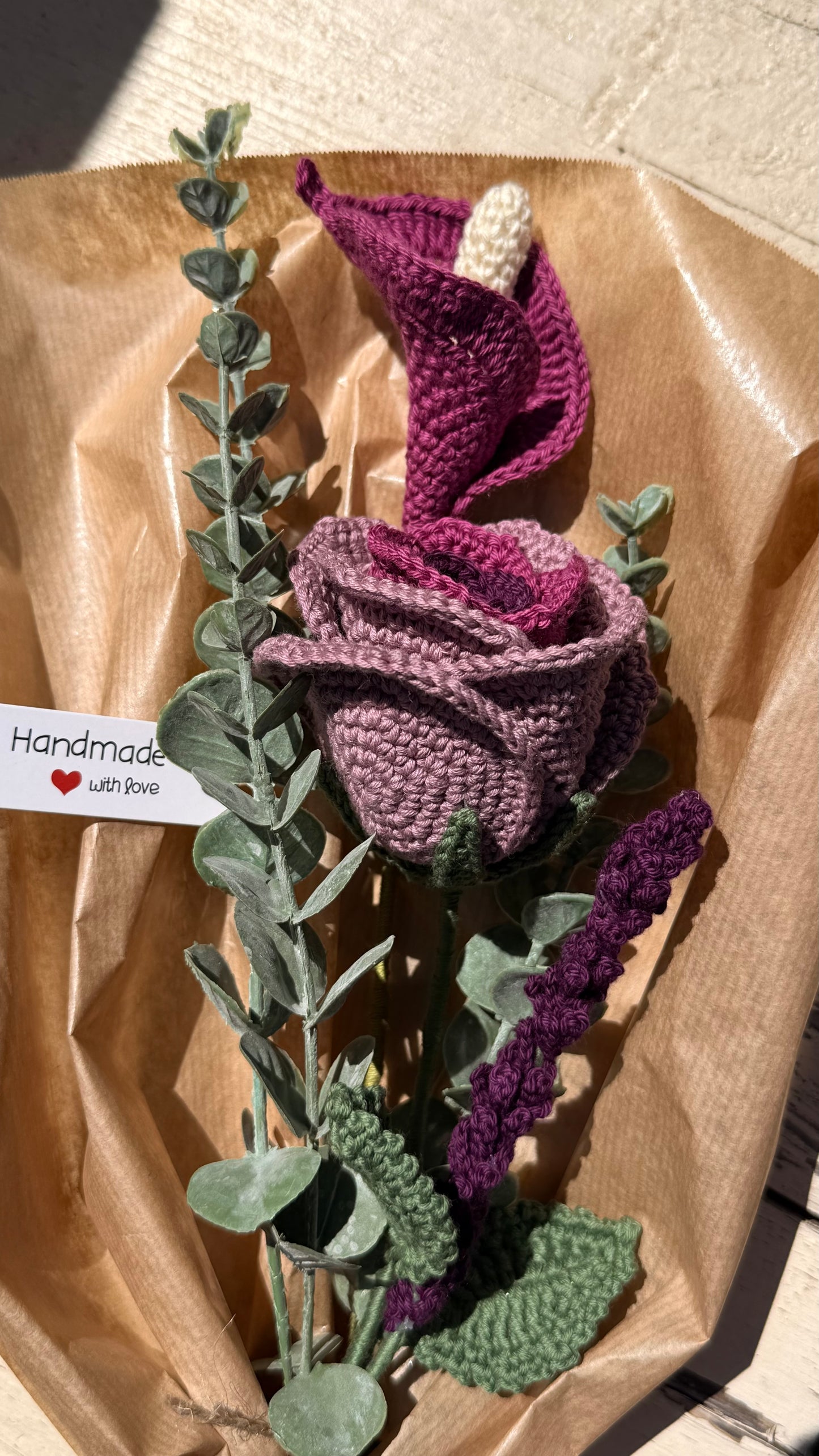 Handgefertigter Blumenstrauß aus der Mama Edeltrud Kollektion mit gehäkelter Calla und Rose in intensiven Beeren- und Violetttönen, elegant verpackt in Naturpapier als nachhaltiges Deko-Geschenk.
