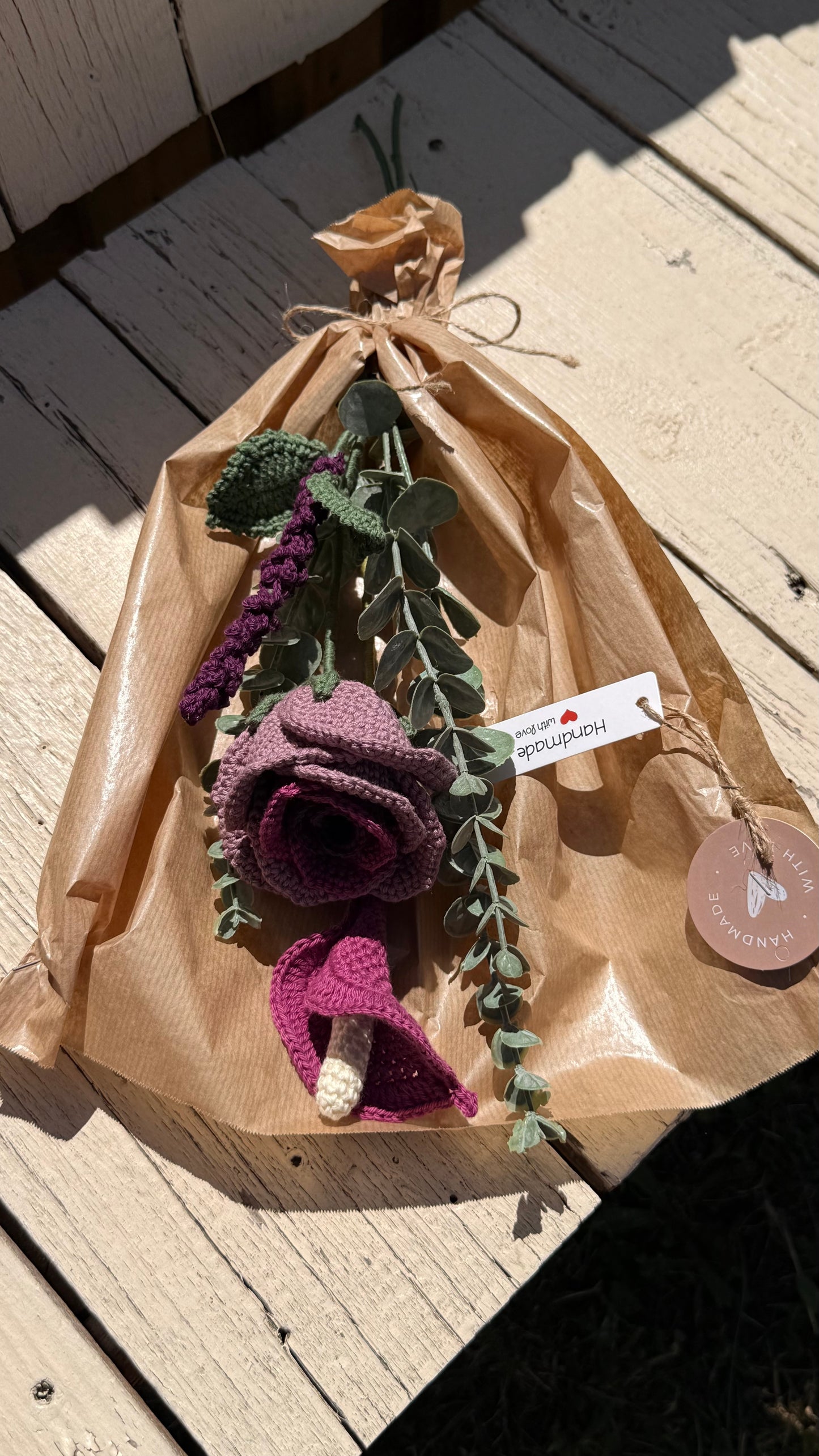 Handgefertigter Blumenstrauß aus der Mama Edeltrud Kollektion mit gehäkelter Calla und Rose in intensiven Beeren- und Violetttönen, elegant verpackt in Naturpapier als nachhaltiges Deko-Geschenk.