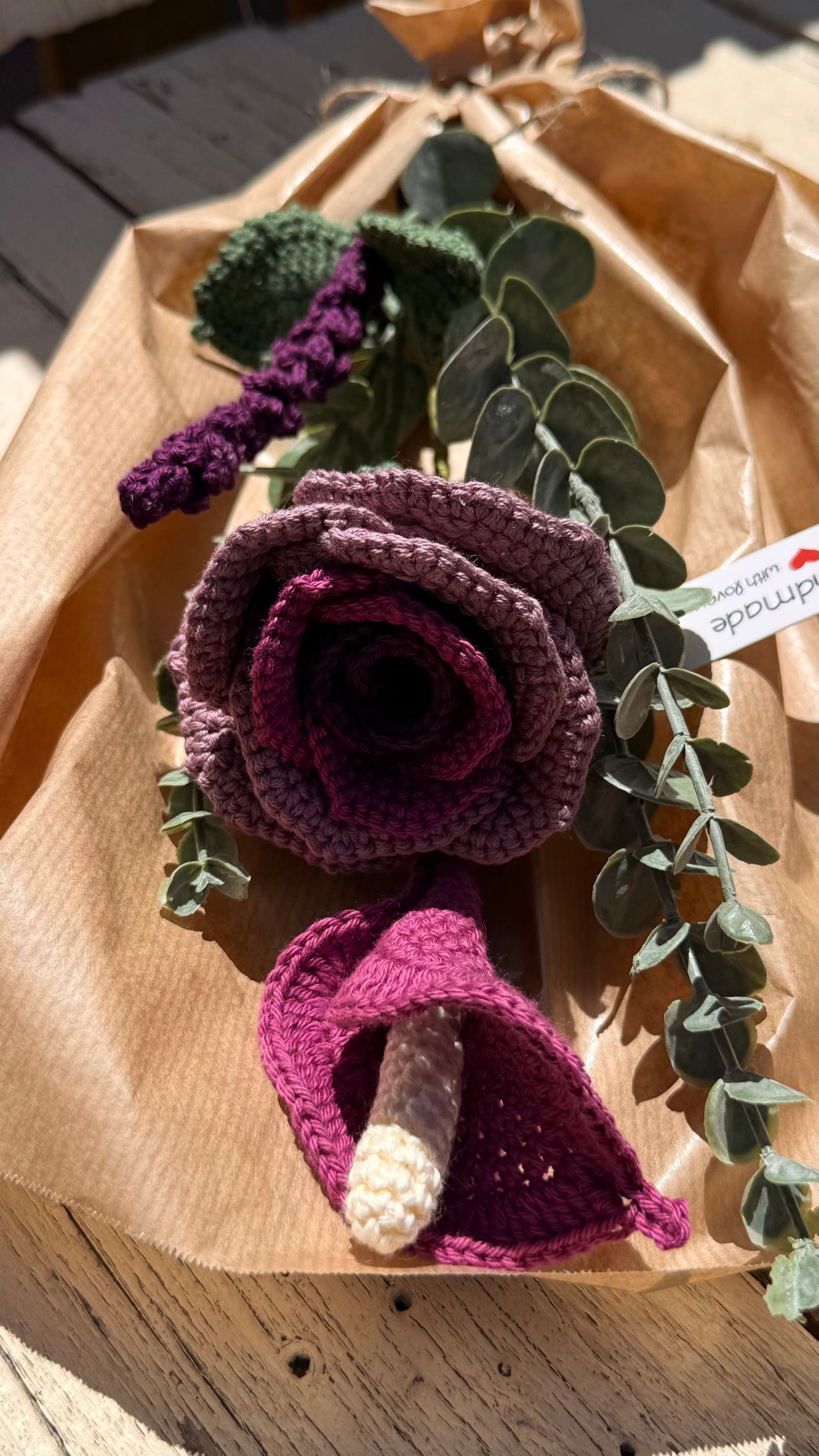 Handgefertigter Blumenstrauß aus der Mama Edeltrud Kollektion mit gehäkelter Calla und Rose in intensiven Beeren- und Violetttönen, elegant verpackt in Naturpapier als nachhaltiges Deko-Geschenk.