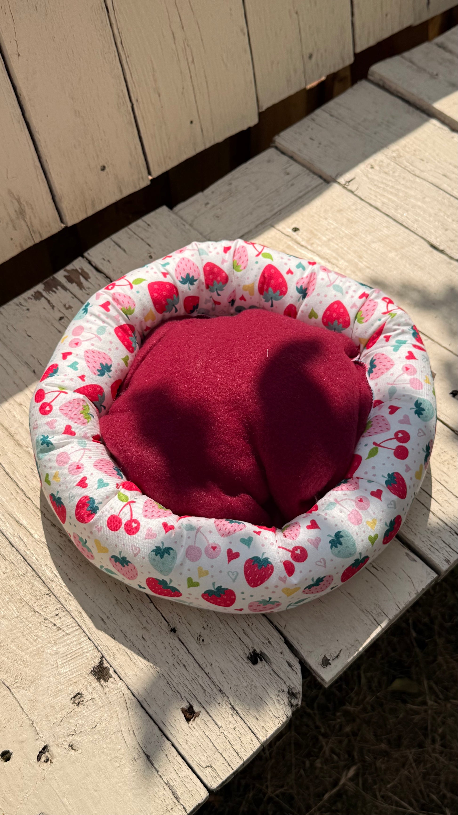 Handgefertigter Kuscheldonut für Meerschweinchen, weiches Kleintierbett mit fröhlichem Erdbeer-, Kirsch- und Herzchen-Muster auf weißem Grund, gemütlicher Rückzugsort aus Dein Krämerladen.