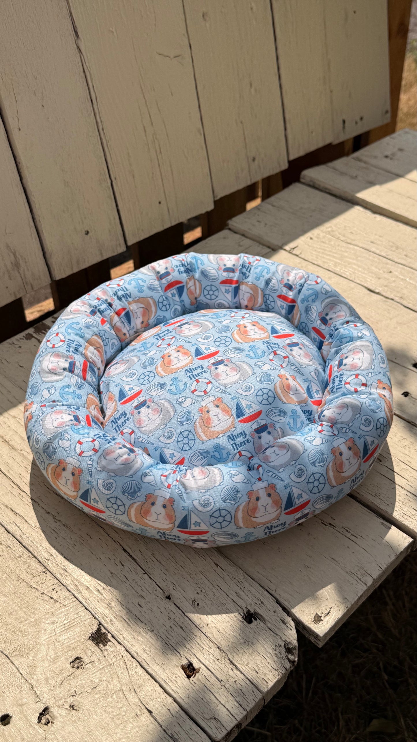 Handgefertigter Kuscheldonut für Meerschweinchen, hellblauer Stoff mit niedlichem Meerschweinchen-Matrosen-Motiv, Segelbooten und Ankern, gemütliches Kleintierbett aus Dein Krämerladen.