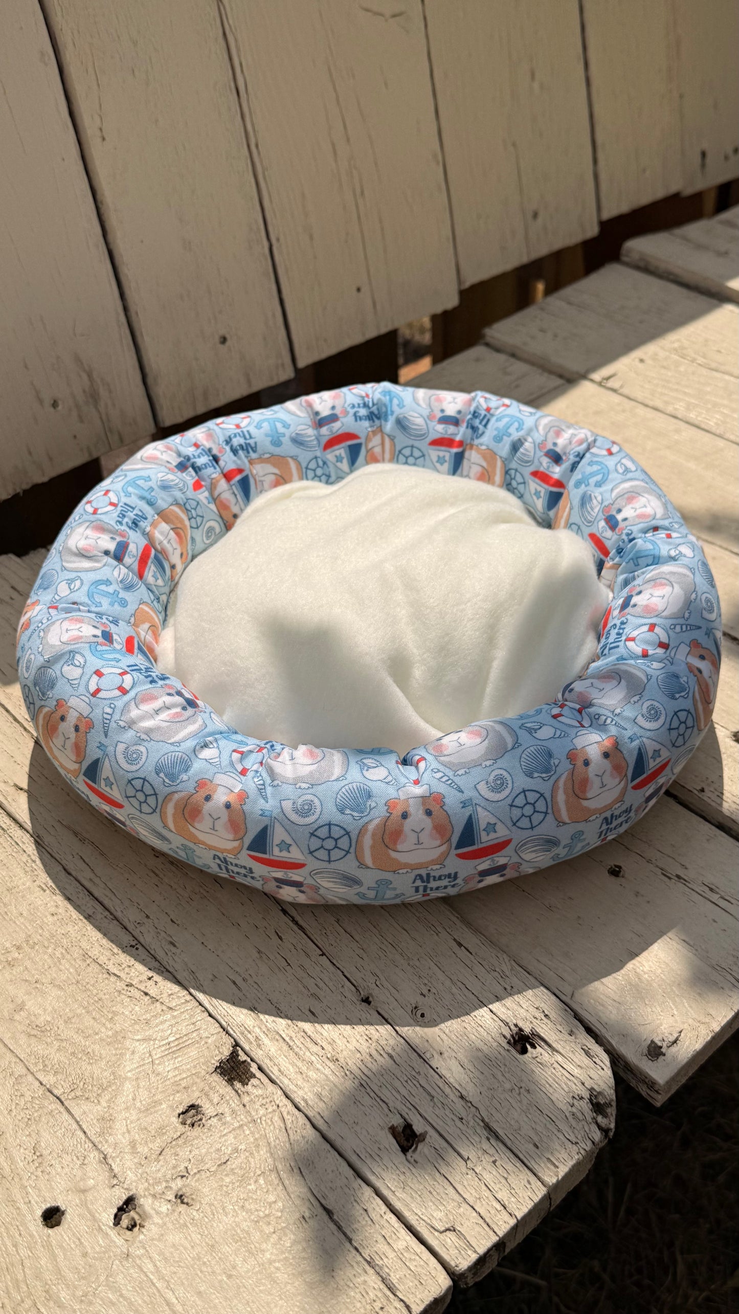 Handgefertigter Kuscheldonut für Meerschweinchen, hellblauer Stoff mit niedlichem Meerschweinchen-Matrosen-Motiv, Segelbooten und Ankern, gemütliches Kleintierbett aus Dein Krämerladen.