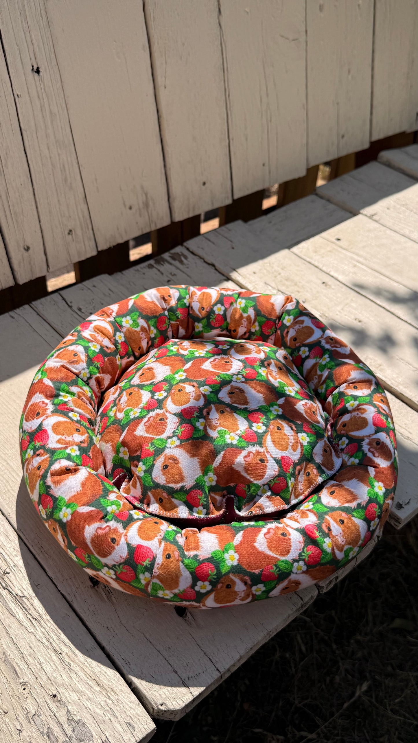 Handgefertigter Kuscheldonut für Meerschweinchen, grüner Stoff mit fotorealistischen Meerschweinchen-Porträts und Erdbeer-Motiven, flauschiges Kleintierbett aus Dein Krämerladen.