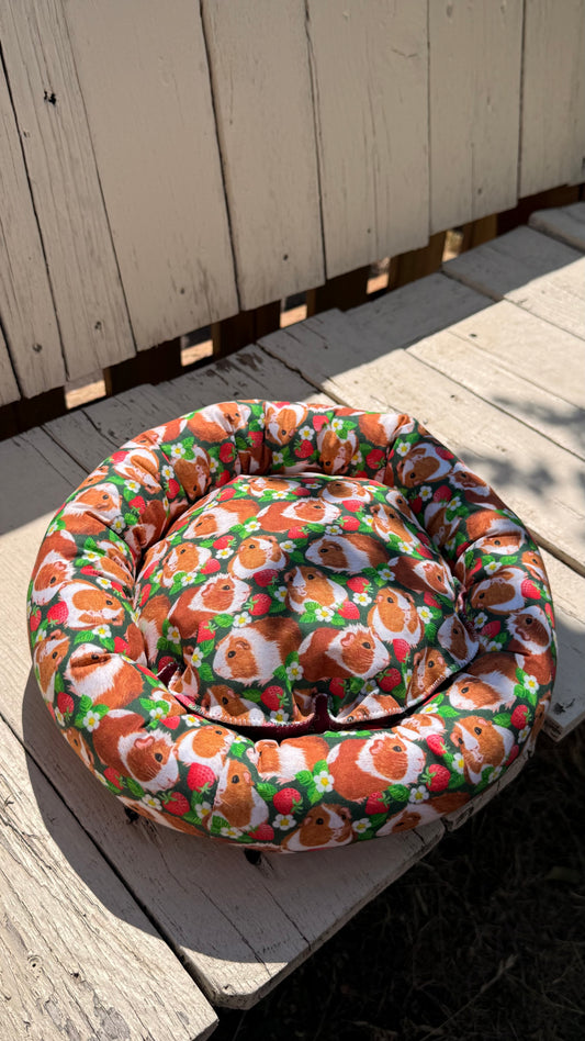 Handgefertigter Kuscheldonut für Meerschweinchen, grüner Stoff mit fotorealistischen Meerschweinchen-Porträts und Erdbeer-Motiven, flauschiges Kleintierbett aus Dein Krämerladen.