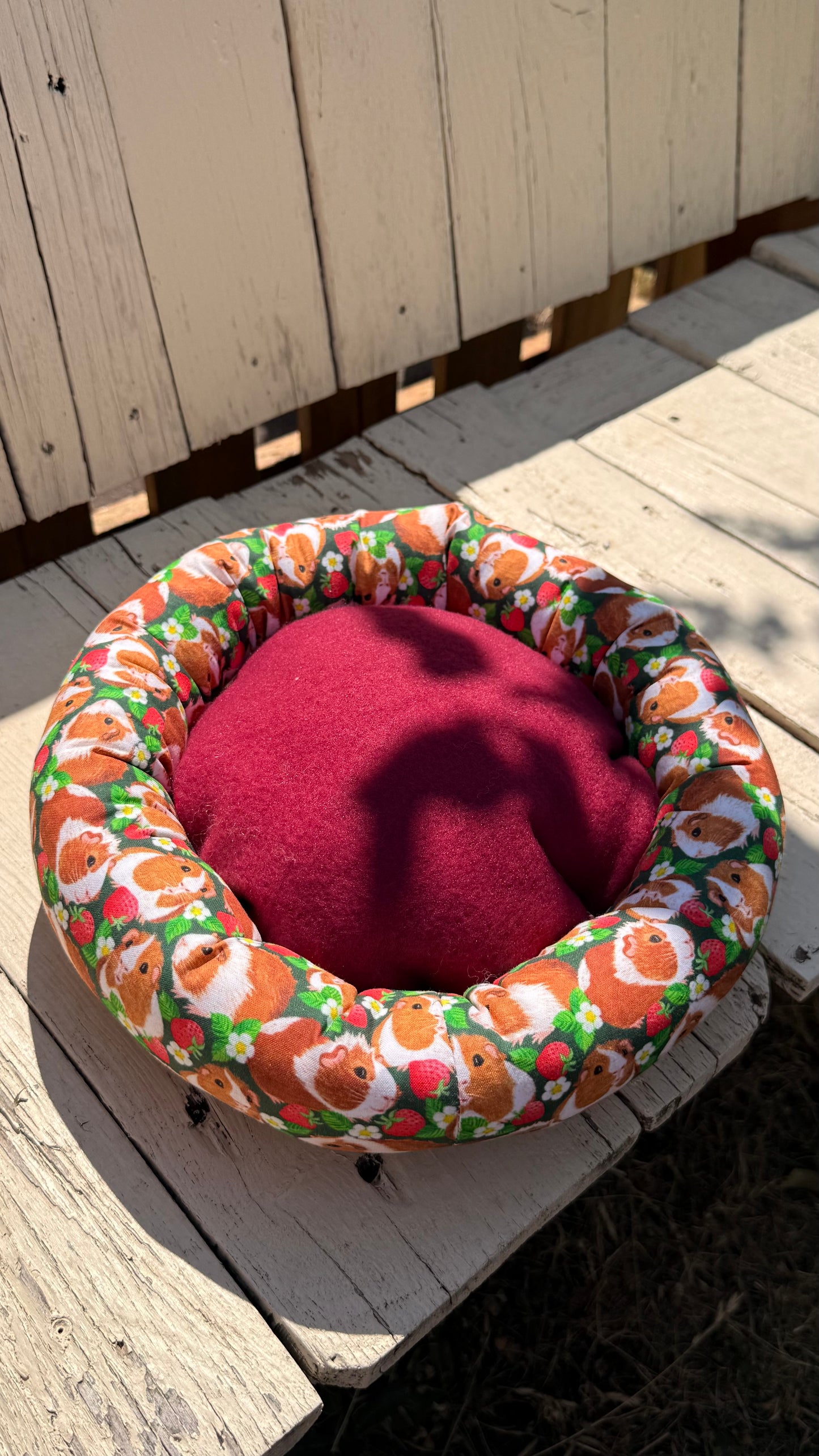 Handgefertigter Kuscheldonut für Meerschweinchen, grüner Stoff mit fotorealistischen Meerschweinchen-Porträts und Erdbeer-Motiven, flauschiges Kleintierbett aus Dein Krämerladen.