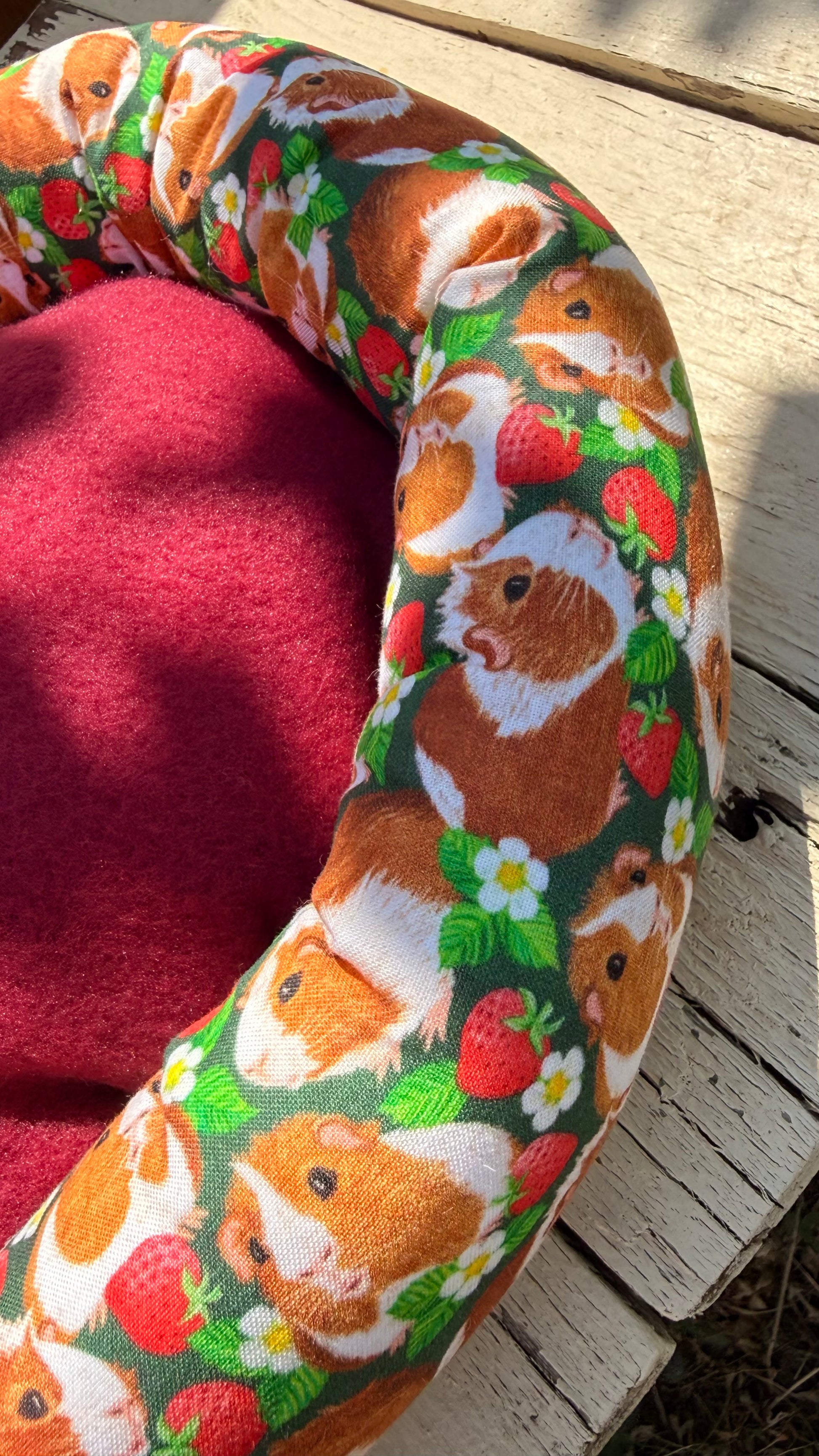 Handgefertigter Kuscheldonut für Meerschweinchen, grüner Stoff mit fotorealistischen Meerschweinchen-Porträts und Erdbeer-Motiven, flauschiges Kleintierbett aus Dein Krämerladen.