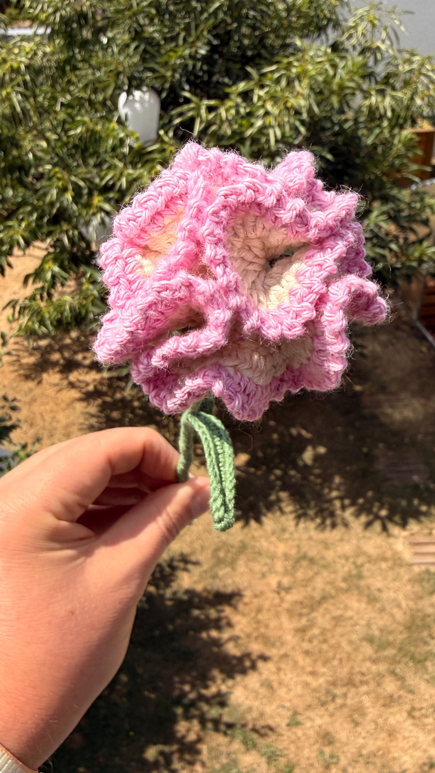 Handgehäkelte Nelke in zartem Rosa und Weiß mit mehrschichtigen Blütenblättern, grünem Stiel und mehreren Blättern, handgemachte Häkelblume aus Dein Krämerladen.