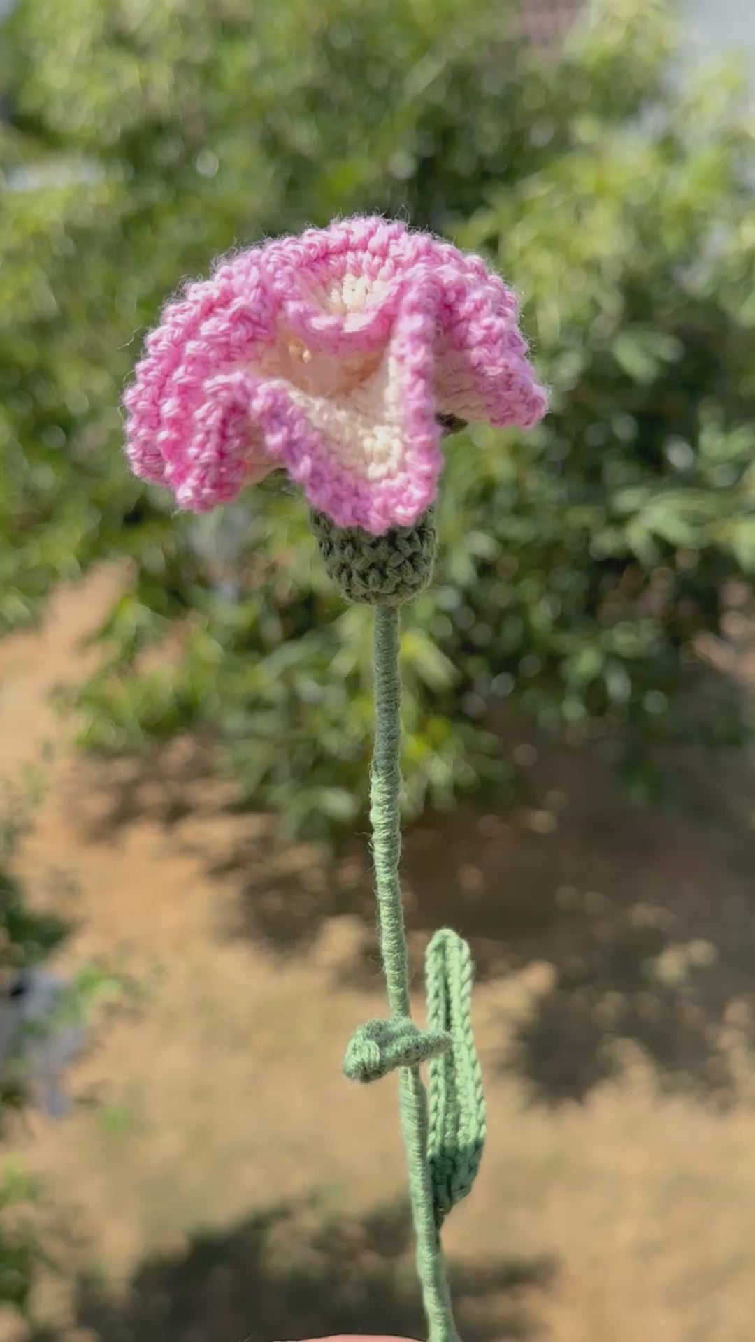 Handgehäkelte Nelke in zartem Rosa und Weiß mit mehrschichtigen Blütenblättern, grünem Stiel und mehreren Blättern, handgemachte Häkelblume aus Dein Krämerladen.