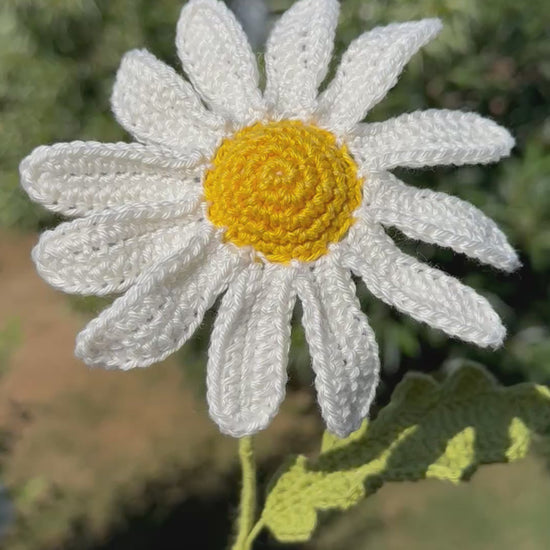 Handgehäkelte Margerite als dekorative Kunstblume, weiße Blütenblätter mit gelbem Kern und grünem Stiel, liebevolle Handarbeit für eine nachhaltige Blumendekoration.