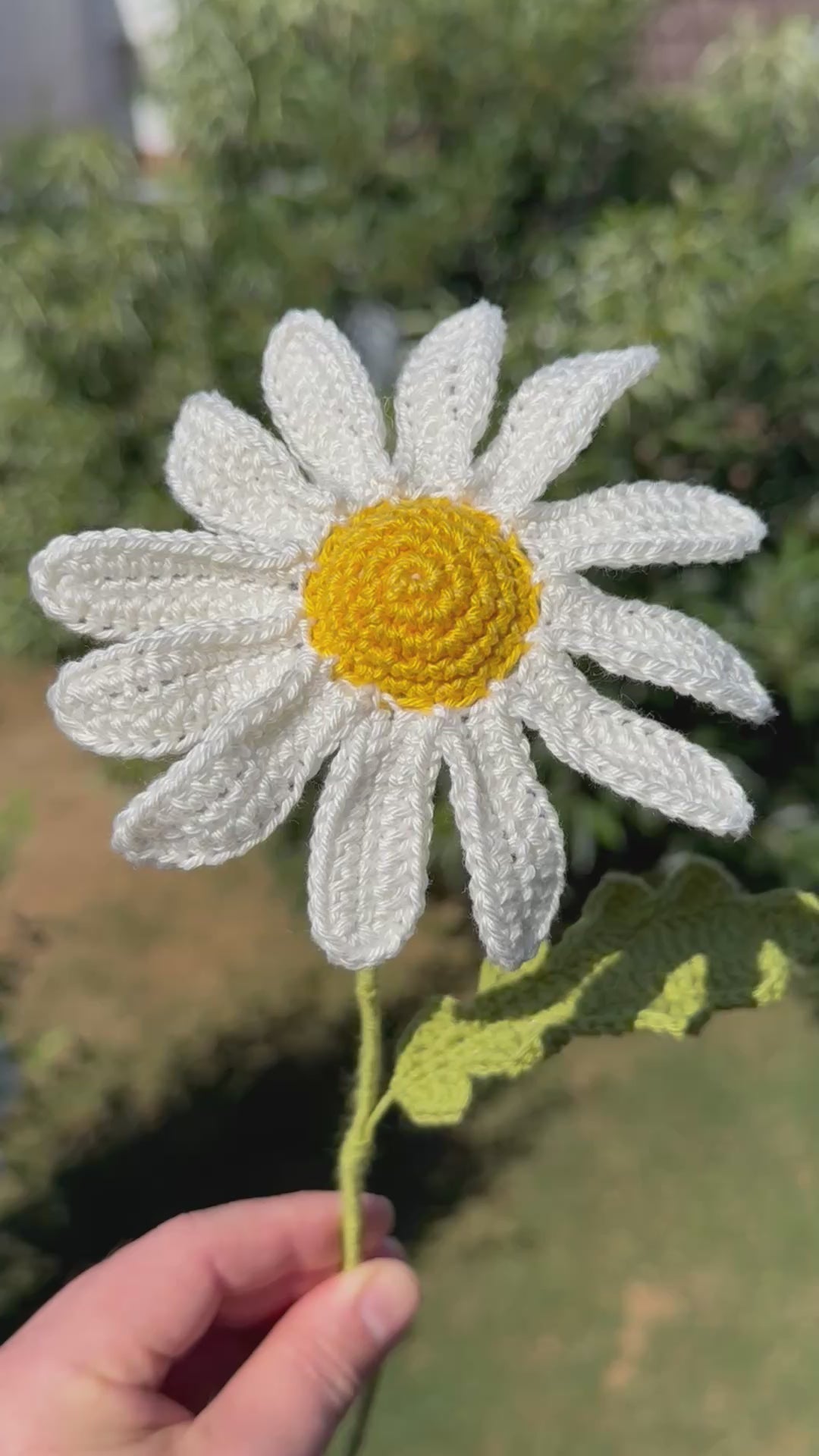 Handgehäkelte Margerite als dekorative Kunstblume, weiße Blütenblätter mit gelbem Kern und grünem Stiel, liebevolle Handarbeit für eine nachhaltige Blumendekoration.